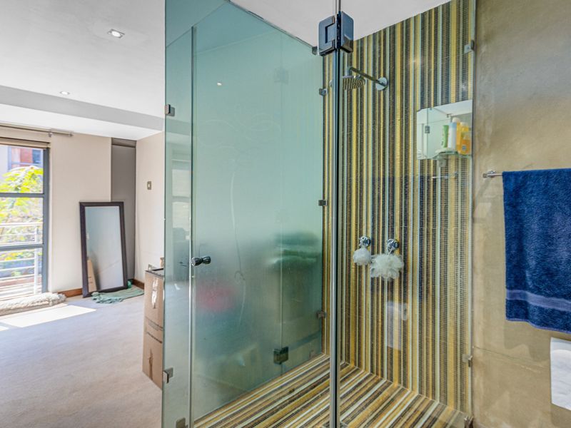 A modern bathroom featuring a glass-enclosed shower with decorative mosaic tiling and recessed ceiling lighting, adjacent to a bright bedroom area.