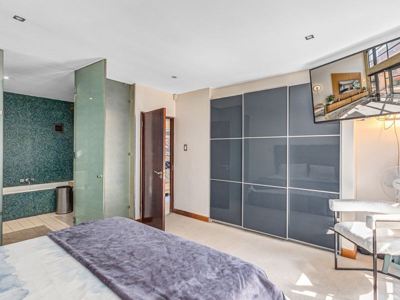 Spacious bedroom featuring modern built-in cupboards and an open-plan en-suite bathroom with a glass partition and decorative mosaic tiling.