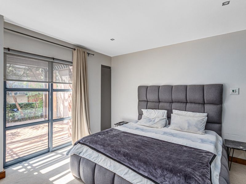 A well-lit bedroom featuring neutral walls, carpeted flooring, recessed downlights, and a large sliding glass door providing access to an outdoor patio area.