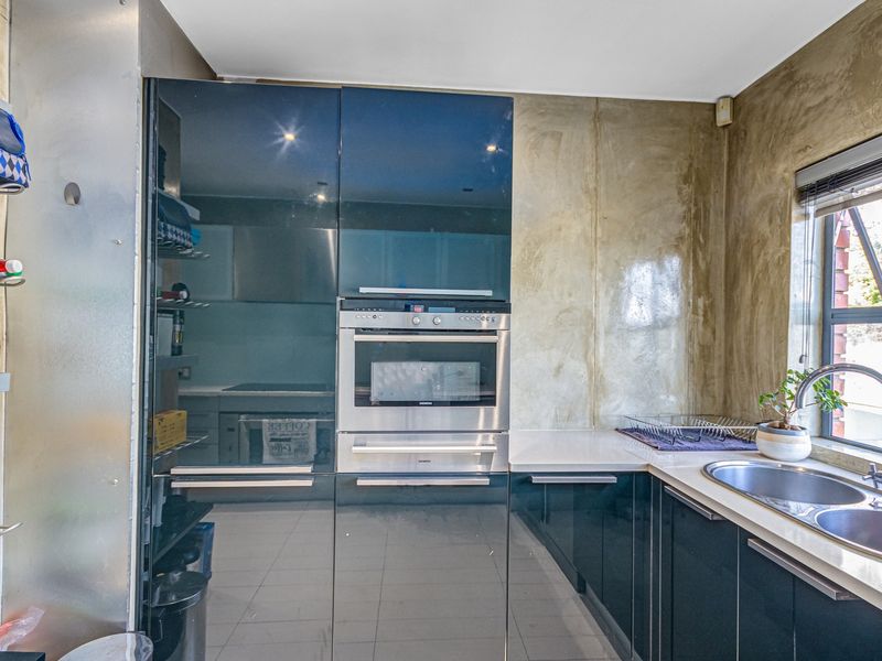 Modern kitchen featuring high-gloss black cabinetry, integrated stainless steel oven, stone countertops, and a polished concrete-style feature wall.