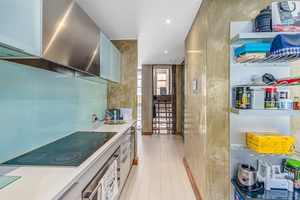 A modern galley-style kitchen featuring a sleek electric cooktop, integrated oven, stainless steel extractor fan, and contemporary glass splashback with tiled flooring.