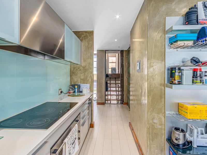 A modern galley-style kitchen featuring a sleek electric cooktop, integrated oven, stainless steel extractor fan, and contemporary glass splashback with tiled flooring.
