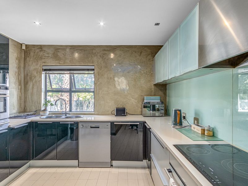 Modern kitchen featuring sleek dark cabinetry, integrated appliances, a glass splashback, and a textured feature wall with ample natural light.