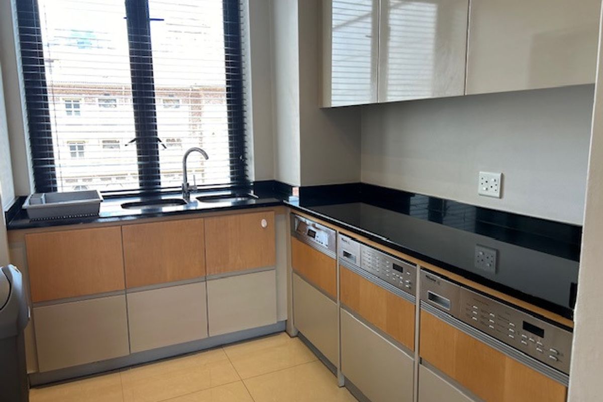 A functional scullery area featuring built-in cabinetry, granite countertops, an integrated dishwasher, and a sink positioned beneath a window.