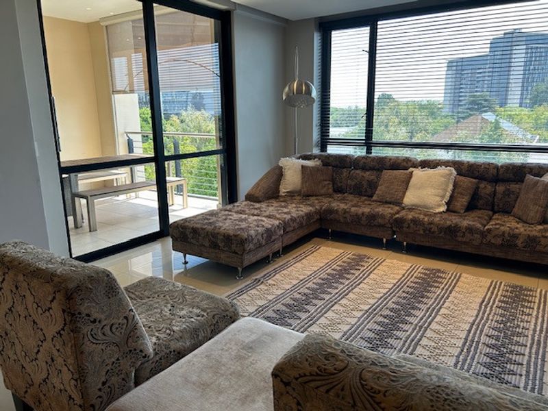Spacious living room featuring large windows, tiled flooring, and sliding glass doors that open onto a private balcony with scenic views.