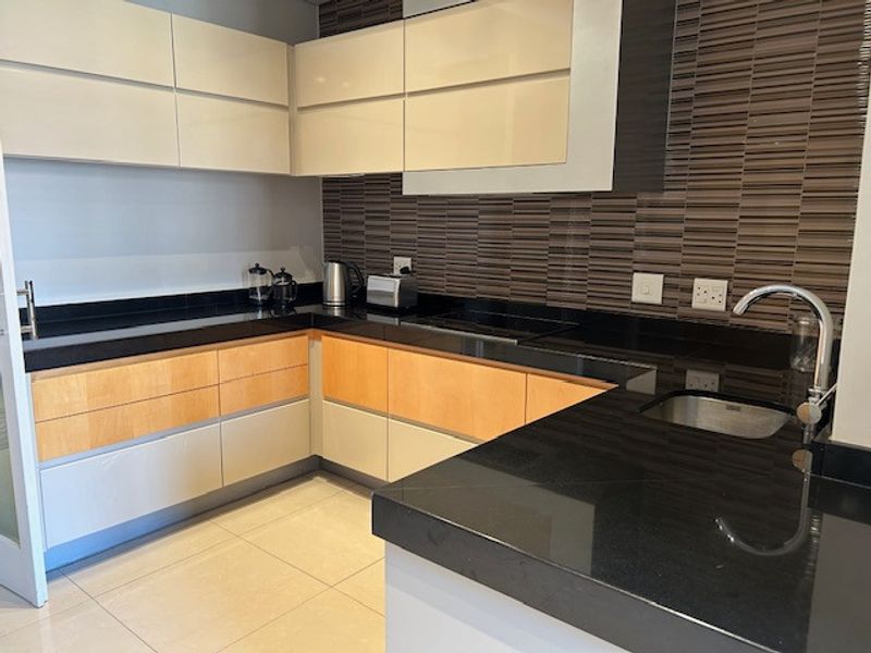 Modern kitchen featuring sleek two-tone cabinetry, black granite countertops, a tiled backsplash, and high-quality floor tiles.