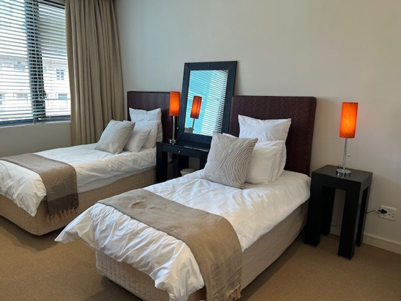 A well-maintained bedroom featuring neutral carpeting, large windows with venetian blinds, and integrated curtain tracks.