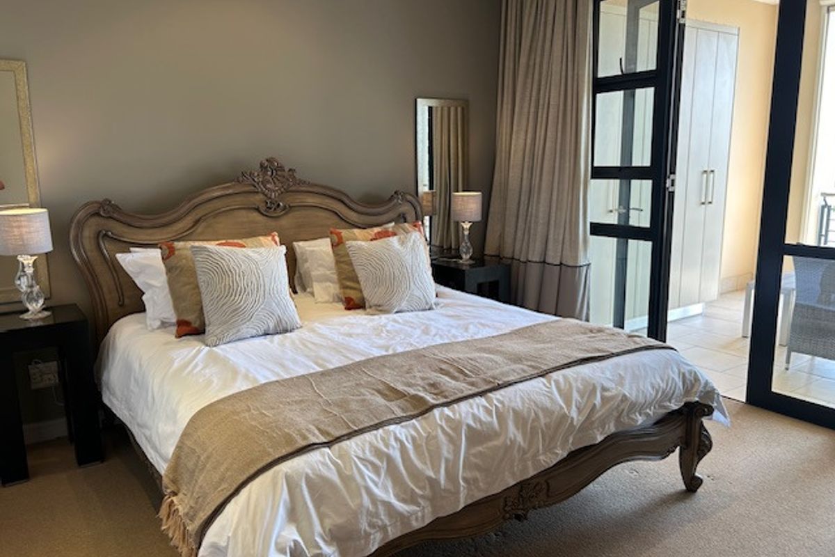 A well-maintained bedroom featuring built-in cupboards, carpeted flooring, and a large sliding glass door providing access to an outdoor balcony area.