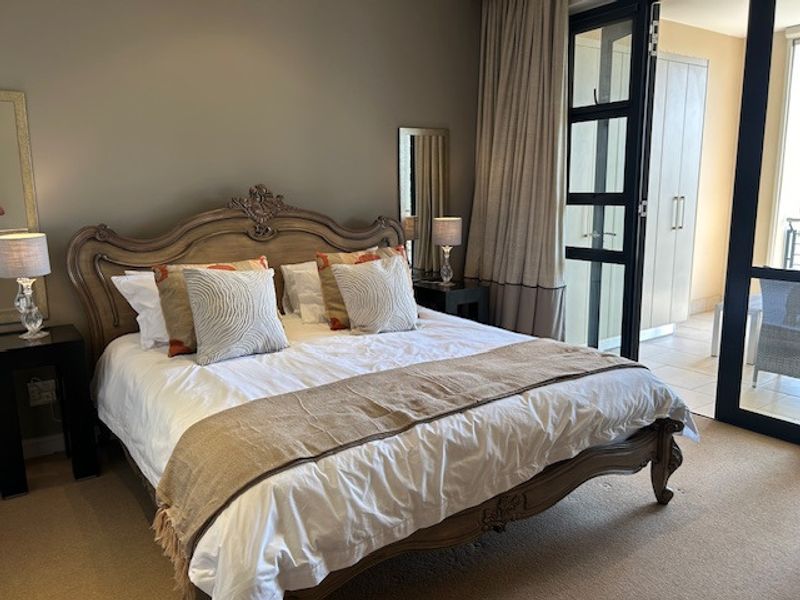 A well-maintained bedroom featuring built-in cupboards, carpeted flooring, and a large sliding glass door providing access to an outdoor balcony area.
