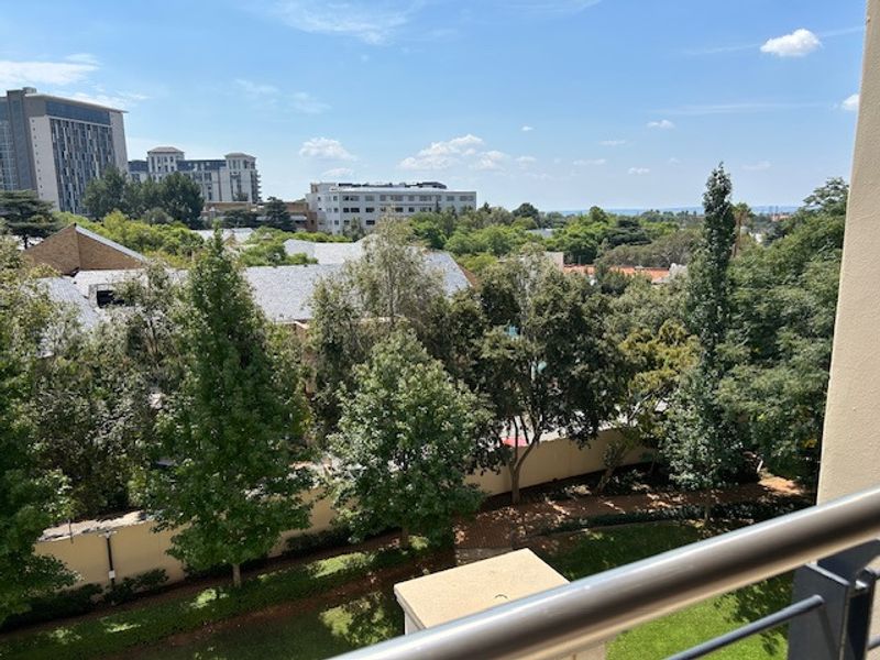 An elevated view overlooking a lush green garden area and surrounding suburban landscape from a balcony.