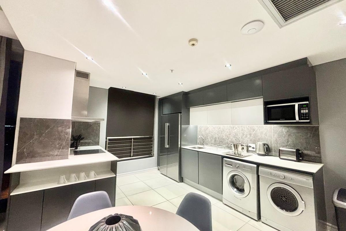Modern kitchen featuring sleek dark cabinetry, stone countertops, integrated appliances, and built-in laundry facilities, finished with high-quality tiling and recessed lighting.