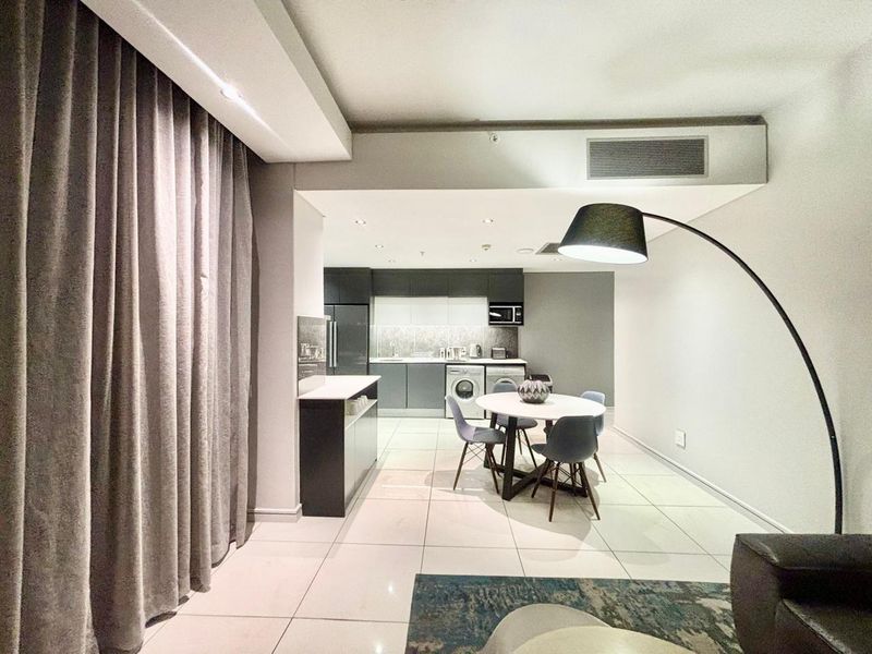 Modern open-plan living area featuring a sleek kitchen with built-in appliances, tiled flooring, and recessed lighting, creating a functional and contemporary hotel suite space.