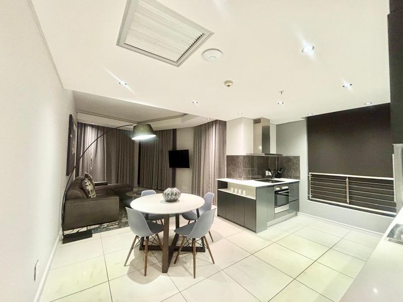 Modern open-plan living area featuring a sleek kitchen with built-in appliances, stone countertops, and bright tiled flooring throughout the combined space.
