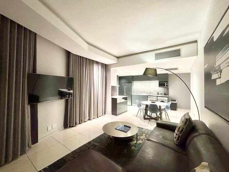 Modern open-plan living area featuring tiled floors, ducted air conditioning, and a sleek, fully equipped kitchen with integrated appliances.