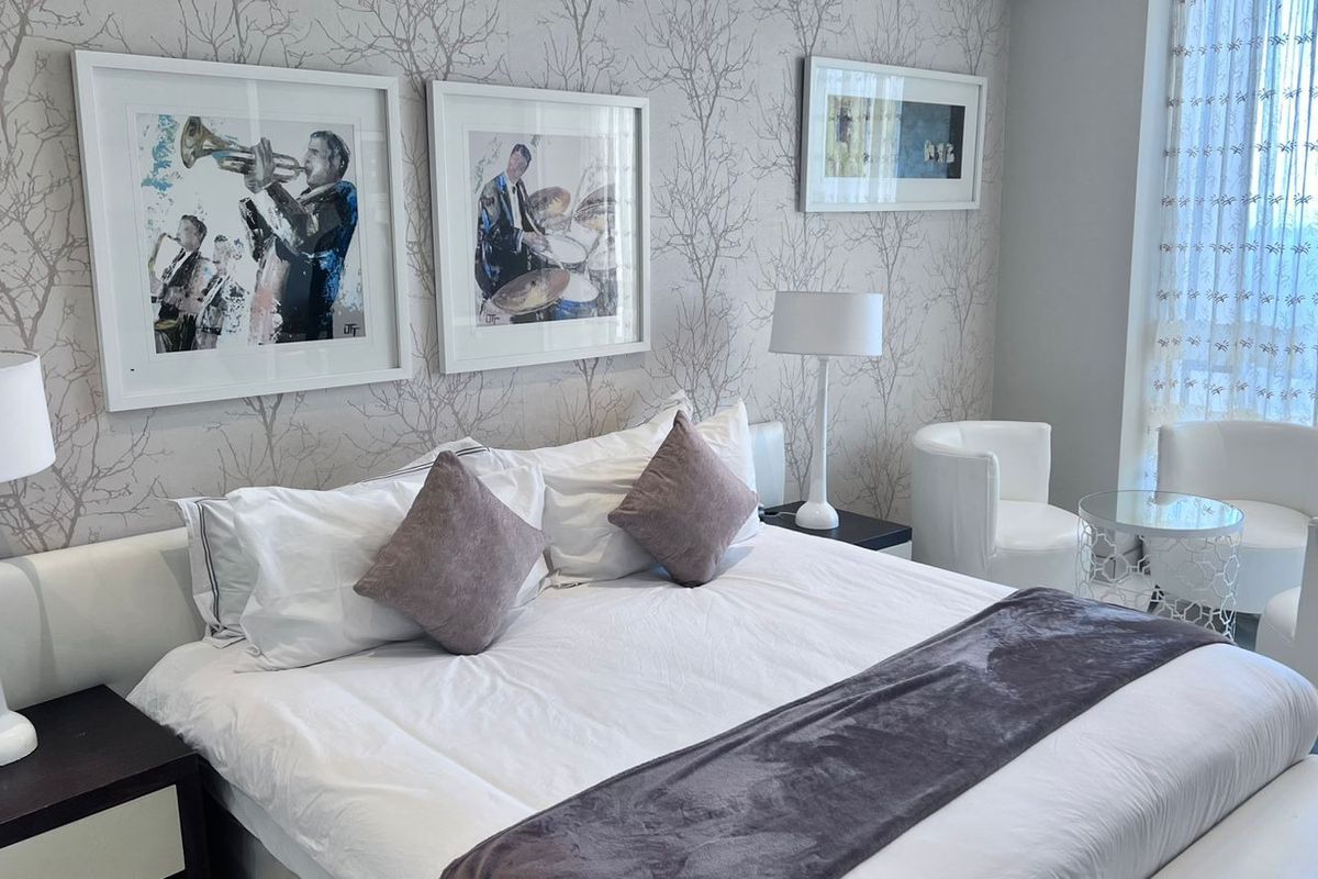 A well-maintained bedroom featuring decorative patterned wallpaper and floor-to-ceiling sheer curtains, creating a bright and comfortable living space.