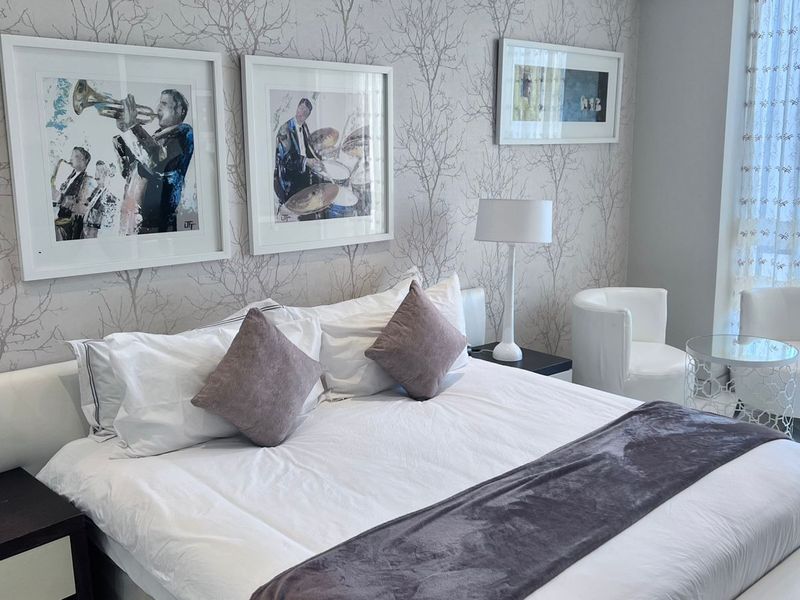 A well-maintained bedroom featuring decorative patterned wallpaper and floor-to-ceiling sheer curtains, creating a bright and comfortable living space.