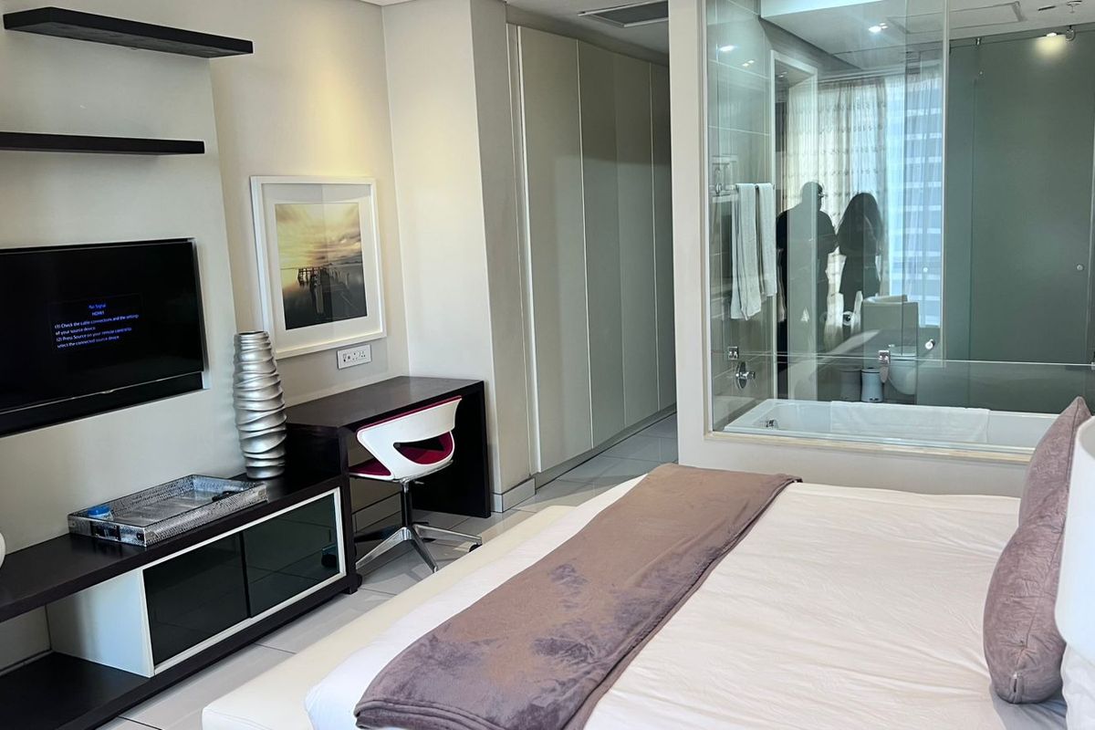 Modern bedroom featuring built-in cabinetry, sleek shelving, and a contemporary glass-enclosed en-suite bathroom with a soaking tub.
