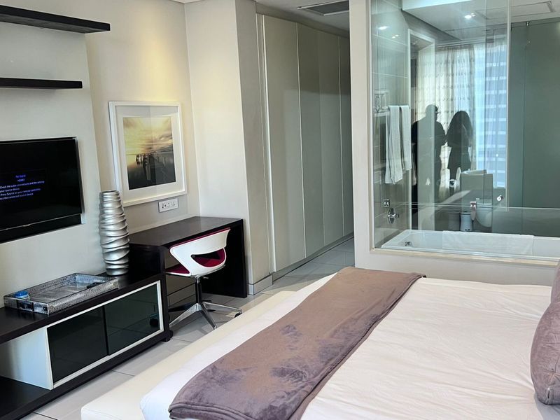 Modern bedroom featuring built-in cabinetry, sleek shelving, and a contemporary glass-enclosed en-suite bathroom with a soaking tub.