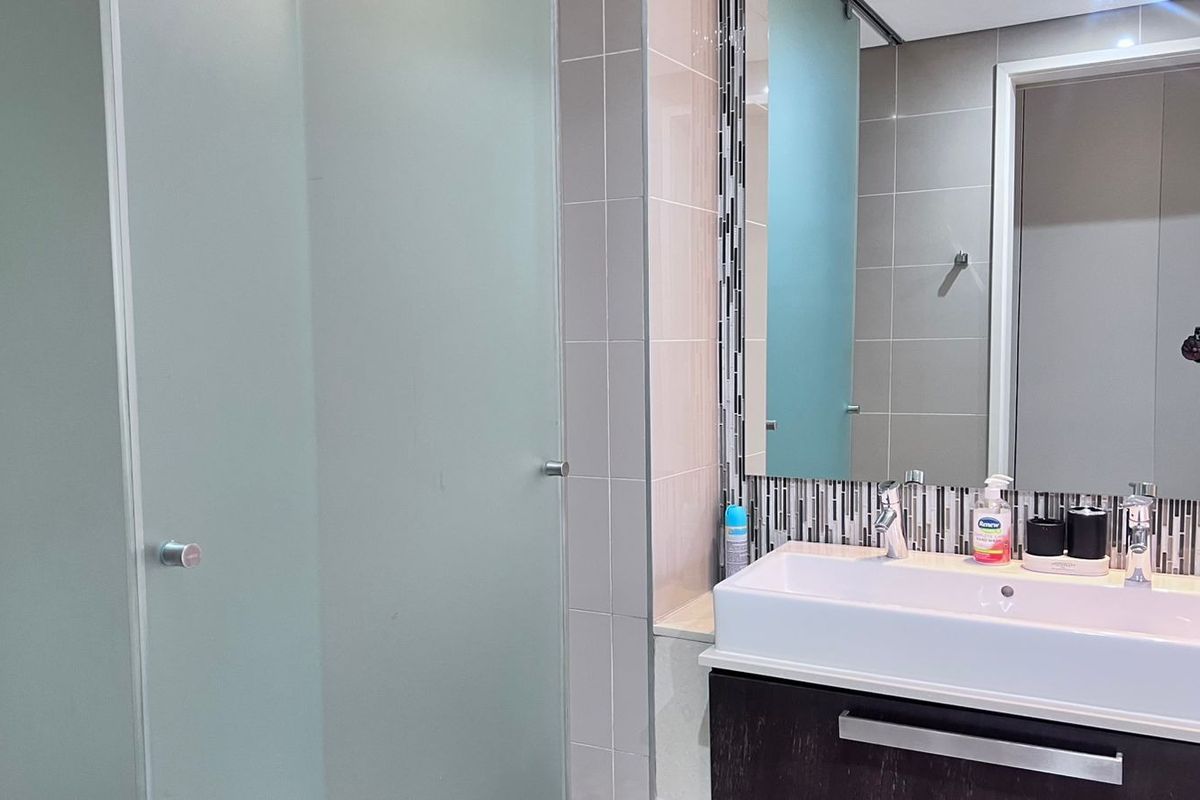 Modern bathroom featuring a dark vanity cabinet with a vessel sink, large wall mirror, mosaic tile backsplash, and a frosted glass door.