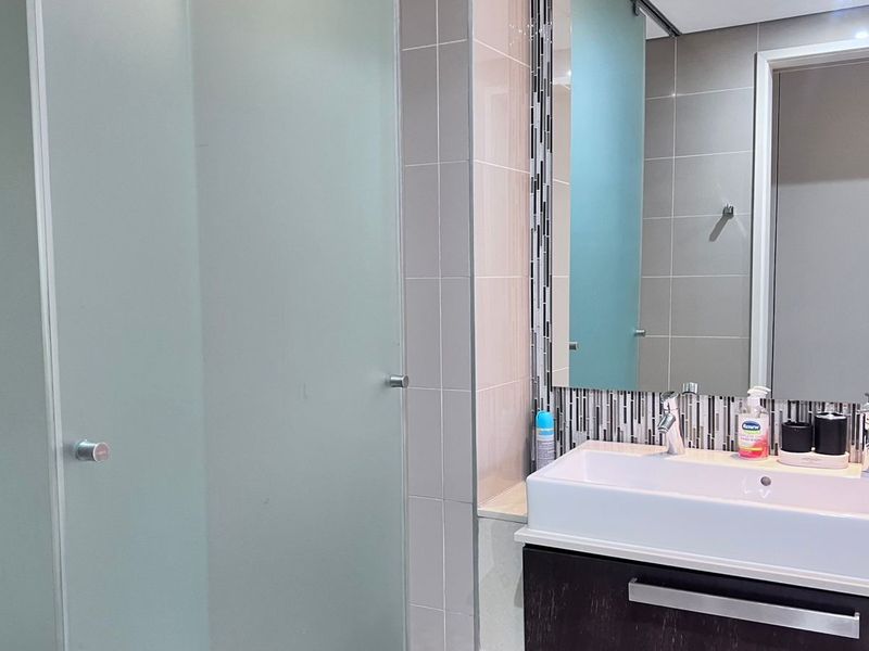 Modern bathroom featuring a dark vanity cabinet with a vessel sink, large wall mirror, mosaic tile backsplash, and a frosted glass door.