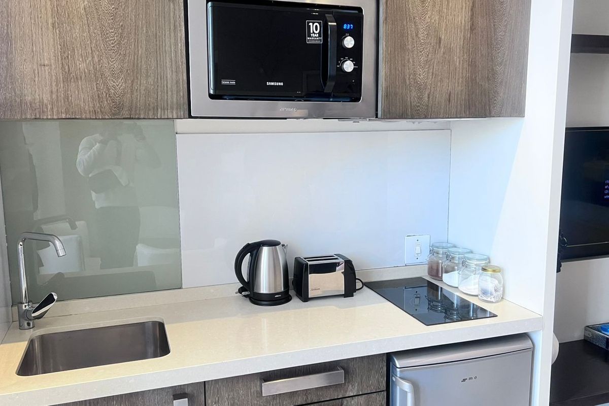 Compact modern kitchen featuring stone countertops, glass splashback, built-in microwave, induction cooktop, and integrated cabinetry with an under-counter refrigerator.