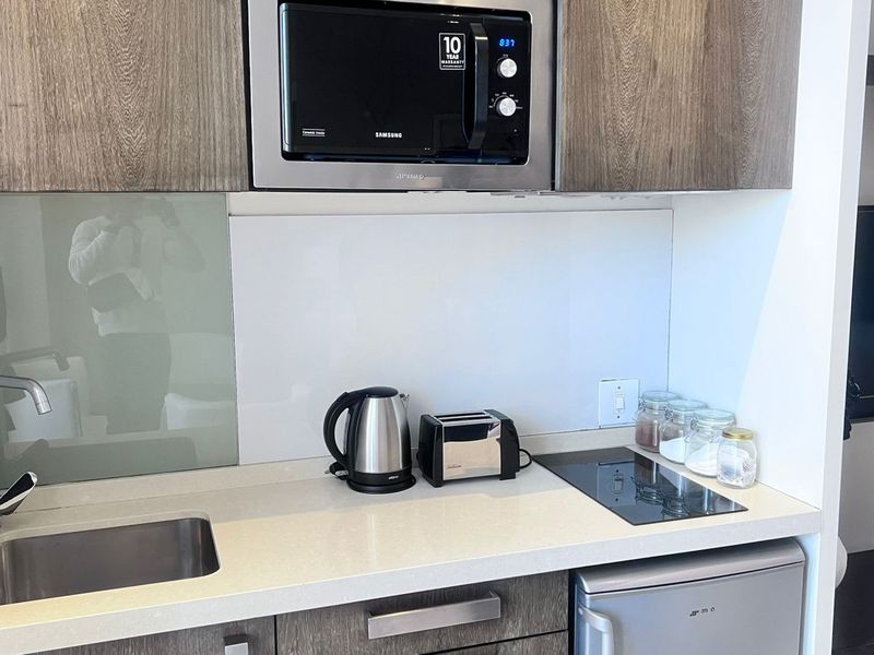Compact modern kitchen featuring stone countertops, glass splashback, built-in microwave, induction cooktop, and integrated cabinetry with an under-counter refrigerator.