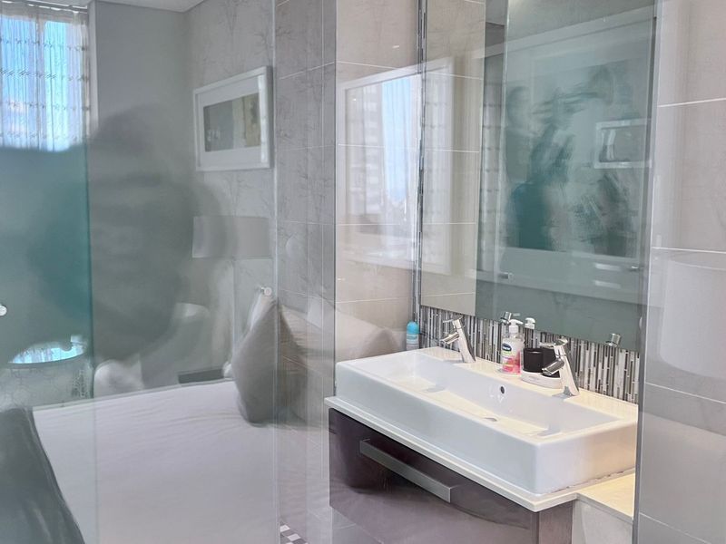 Modern bathroom featuring a wall-mounted toilet, sleek vanity cabinet with a ceramic basin, and a glass shower screen with tiled wall finishes.