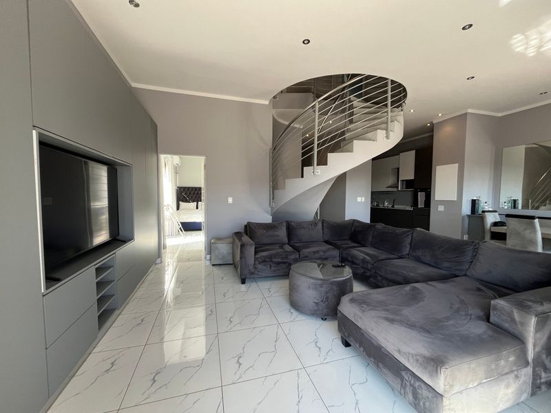 Modern open-plan living area featuring a striking spiral staircase, sleek built-in cabinetry, and polished marble-look floor tiles with recessed lighting throughout.