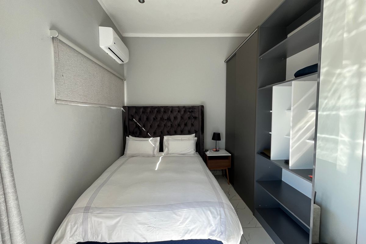 A compact bedroom featuring tiled flooring, a built-in wardrobe, and a wall-mounted split-system air conditioner.