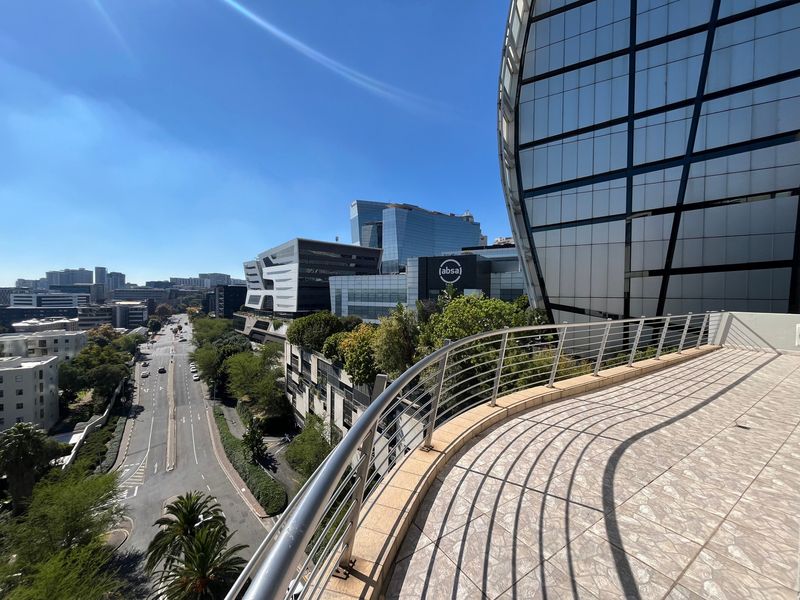 A spacious curved balcony featuring tiled flooring and a metal balustrade, offering an elevated urban view of the surrounding city skyline.