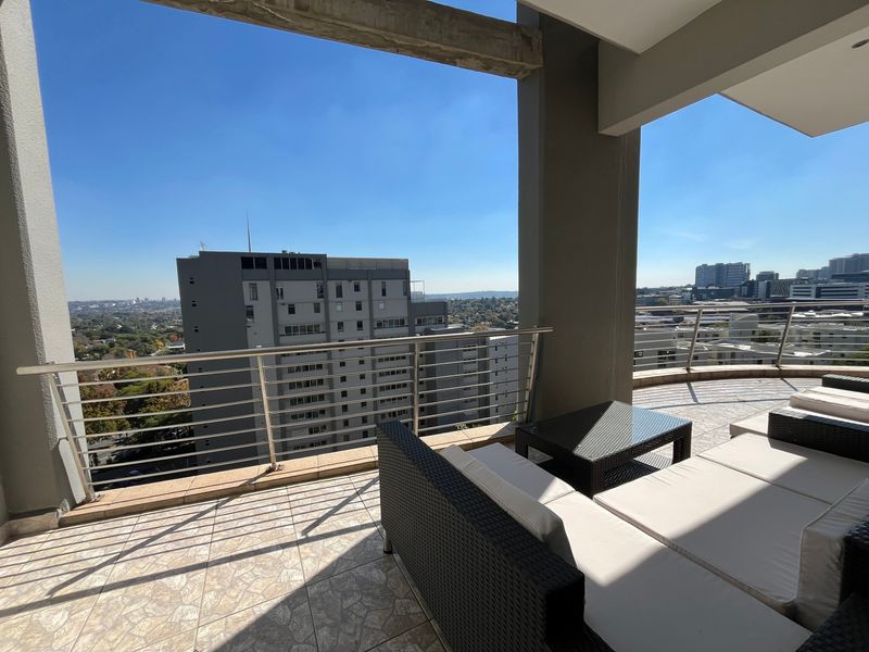 Spacious covered balcony featuring tiled flooring and a modern stainless steel balustrade, offering expansive urban views.