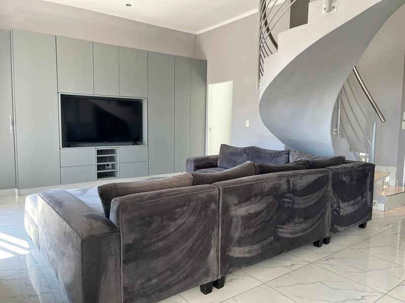 Modern living room featuring sleek built-in cabinetry, polished marble-look tiled flooring, and a striking spiral staircase with a contemporary metal handrail.