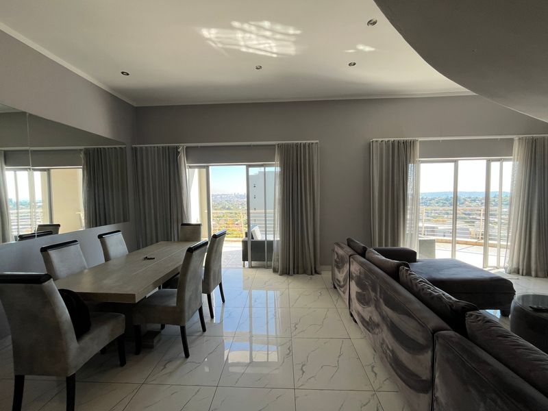 Spacious open-plan living and dining area featuring large format marble-look floor tiles, recessed lighting, and dual sliding glass doors leading to a balcony.