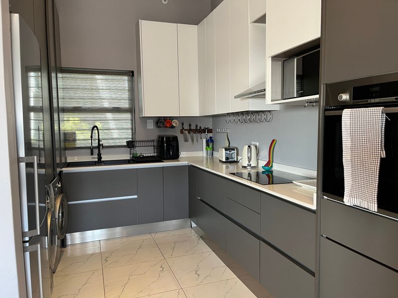 Modern kitchen featuring sleek two-tone cabinetry, quartz countertops, integrated appliances including an oven and induction hob, and contemporary tiled flooring.