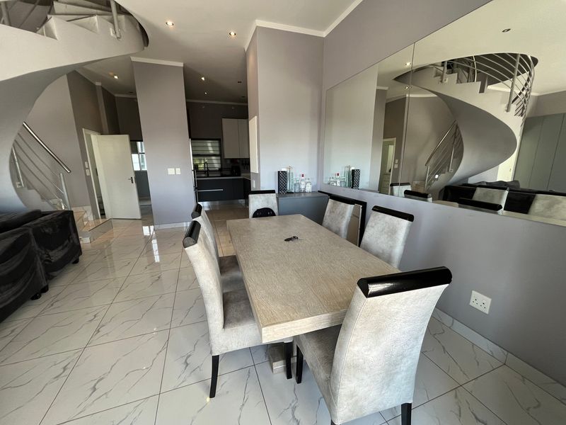 Open-plan dining area featuring modern porcelain floor tiles, a striking spiral staircase with stainless steel handrails, and a large feature wall mirror.