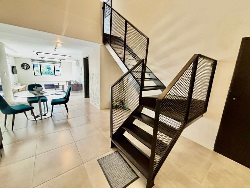 Open plan living area featuring a modern industrial-style metal staircase with mesh balustrades and neutral tiled flooring throughout.