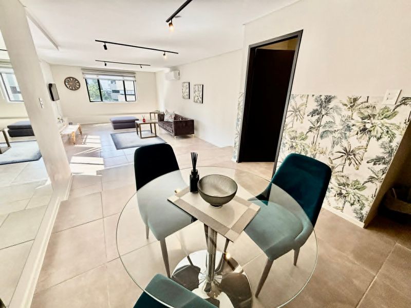 Spacious open-plan living and dining area featuring modern track lighting, neutral tiled flooring, and a decorative botanical wallpaper feature wall.