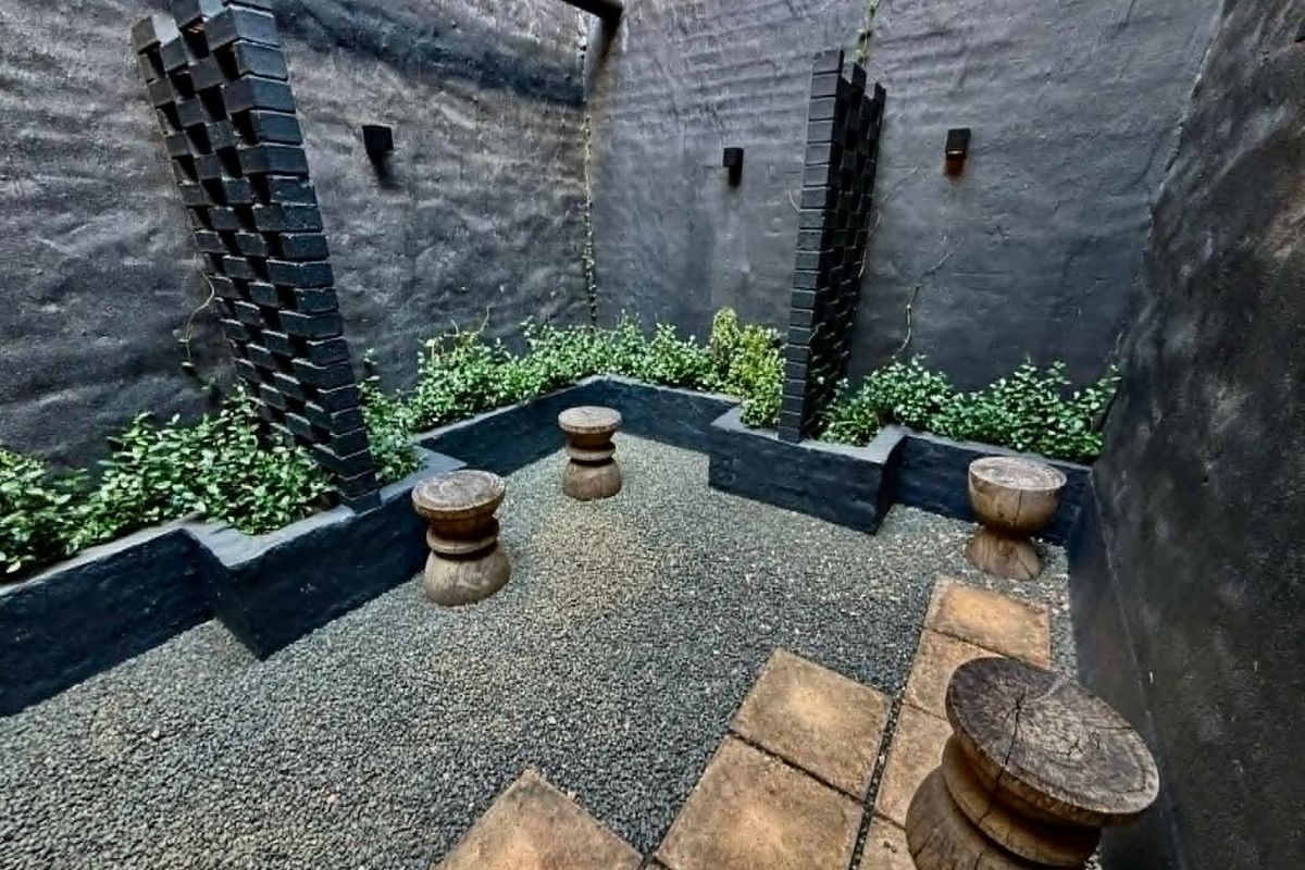 A private, enclosed rear courtyard featuring dark painted brick walls, built-in planter boxes, gravel ground cover, and stone paving accents.