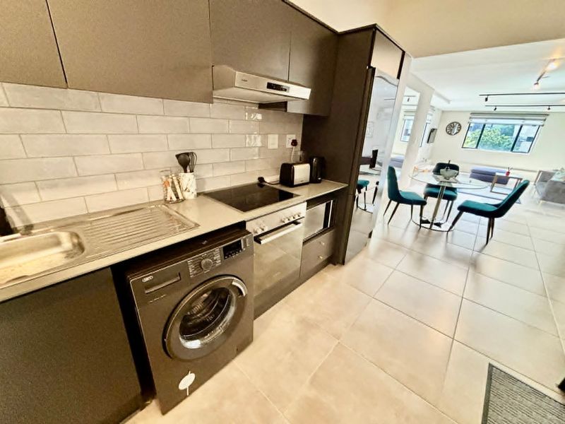 Modern open-plan kitchen featuring sleek dark cabinetry, subway tile backsplash, integrated appliances, and seamless flow into the adjacent dining and living area.