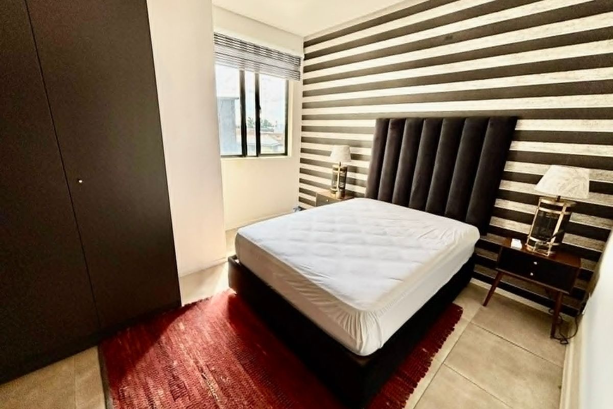 A well-lit bedroom featuring tiled flooring, a built-in wardrobe, and a window with a fitted blind.