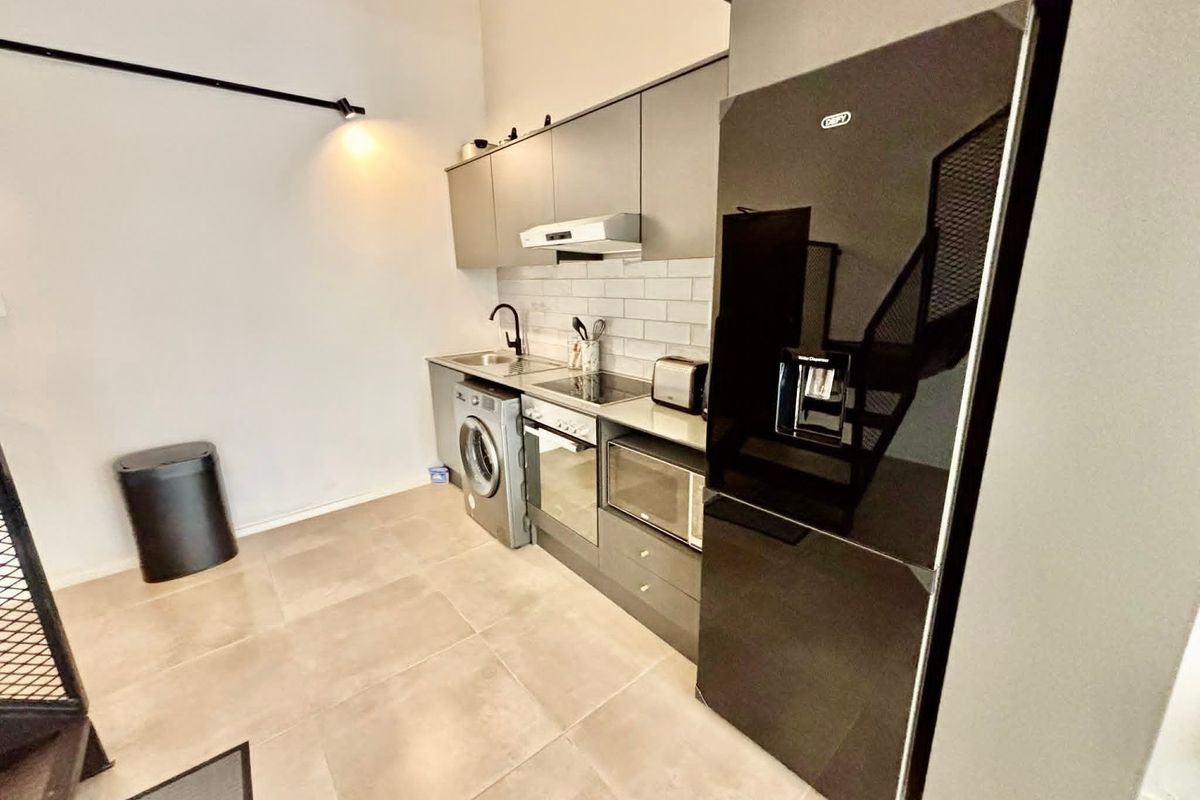 Modern kitchen featuring sleek grey cabinetry, subway tile backsplash, integrated appliances, and tiled flooring in an open-plan layout.