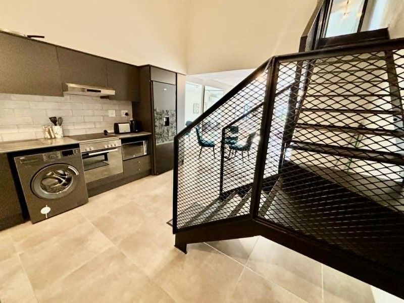 Modern open-plan kitchen featuring sleek dark cabinetry, integrated appliances, subway tile backsplash, and a striking industrial-style metal staircase.