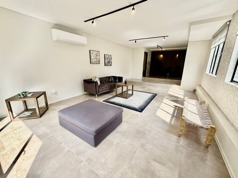 Spacious living area featuring modern track lighting, neutral tiled flooring, and a wall-mounted air conditioning unit.
