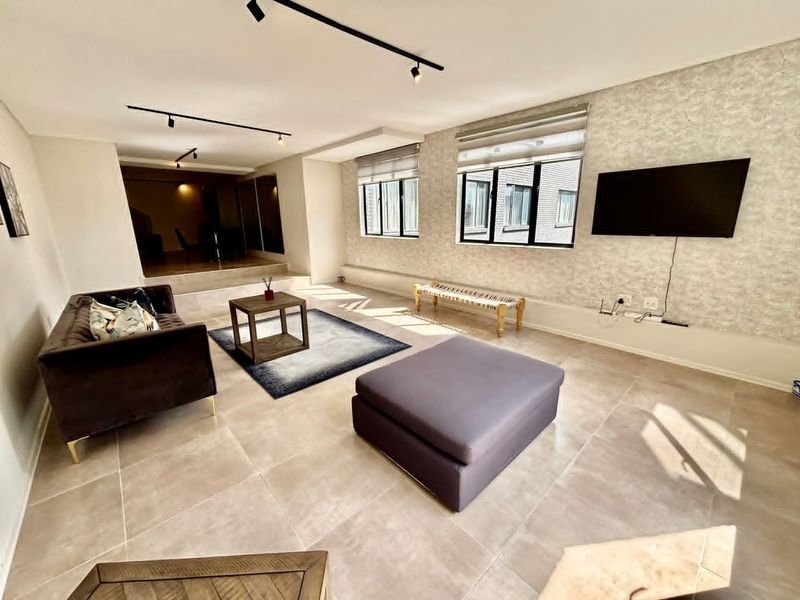 Spacious living room featuring large format floor tiles, modern track lighting, and textured feature wall with integrated television mounting point.