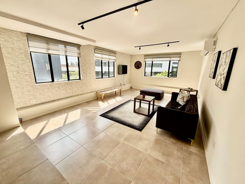 A bright and spacious living room featuring neutral tiled flooring, modern track lighting, textured feature walls, and split-system air conditioning.