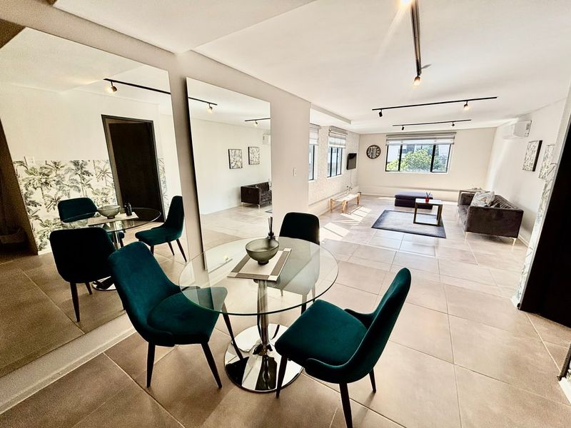 Spacious open-plan living and dining area featuring large wall mirrors, modern track lighting, and neutral tiled flooring throughout.
