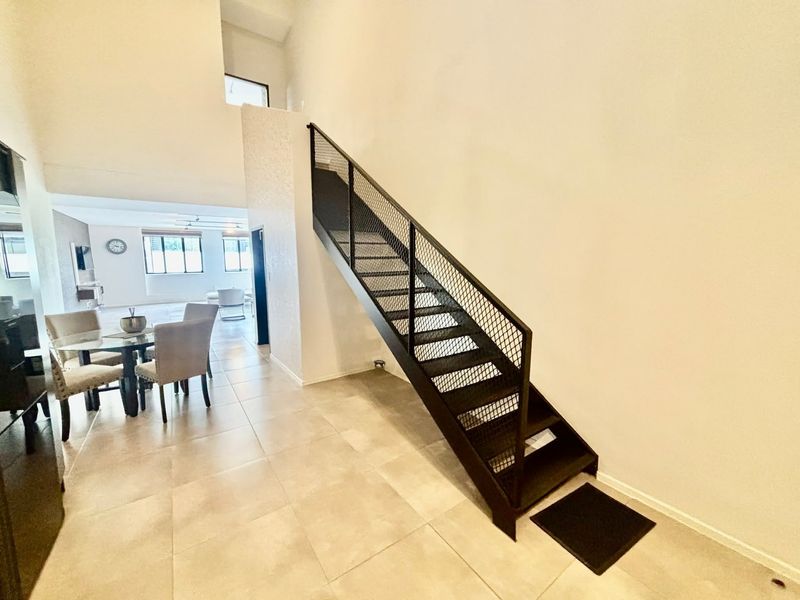 Open plan living area featuring a modern industrial-style metal staircase with mesh balustrade, tiled flooring, and impressive double volume ceilings.
