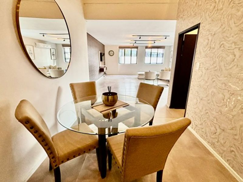 Spacious open-plan living and dining area featuring modern track lighting, neutral tiled flooring, and elegant textured wallpaper accents.