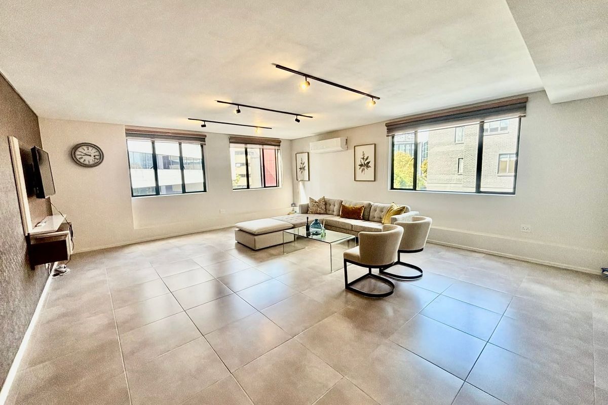 Spacious living area featuring large windows, neutral tiled flooring, modern track lighting, and a wall-mounted air conditioning unit.