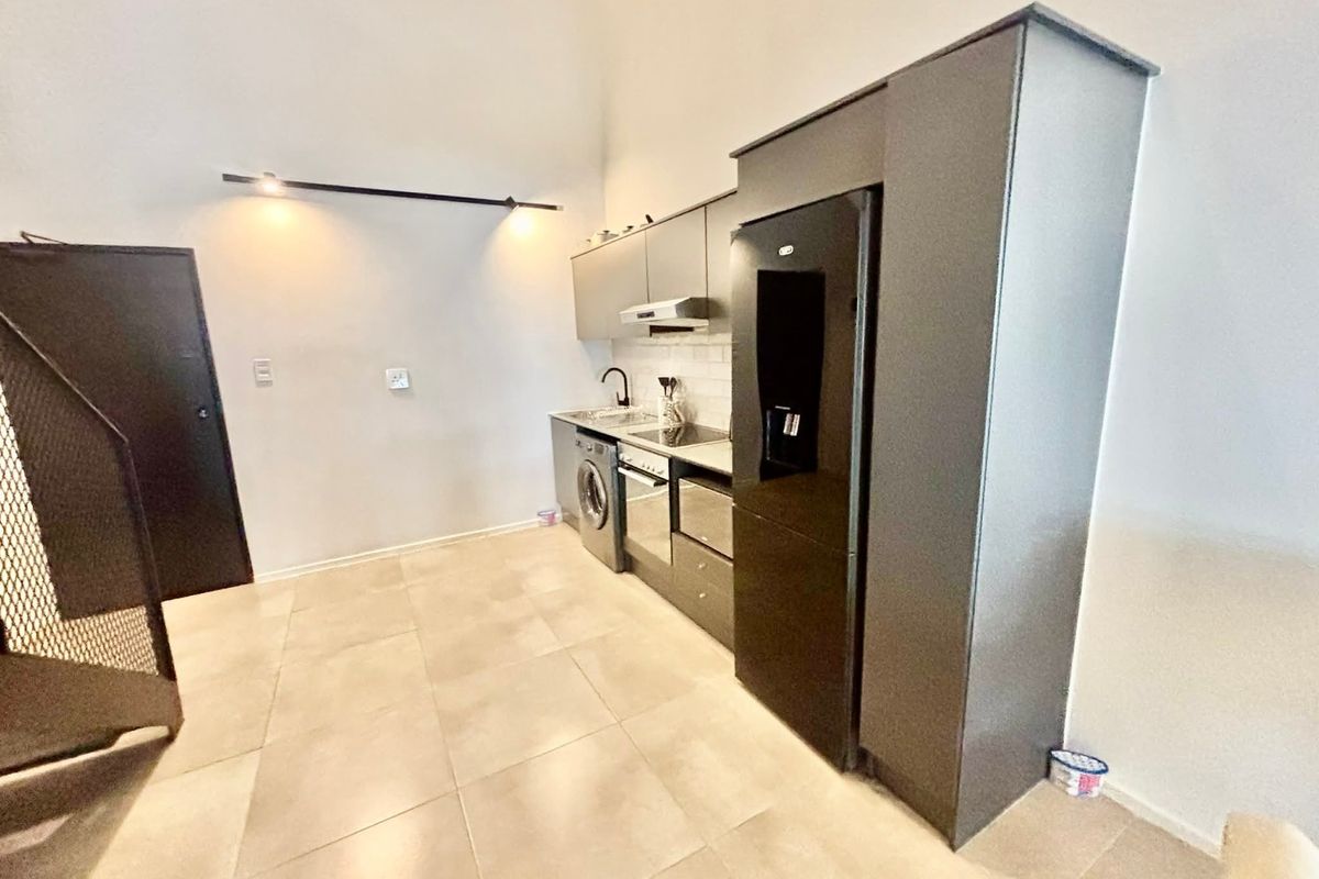 Modern kitchen featuring sleek grey cabinetry, integrated appliances, tiled flooring, and contemporary track lighting in an open-plan layout.